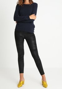 Granatowy sweter o fakturze, dopasowane czarne legginsy i żółte czółenka na obcasie z wysmukłymi akcentami. Prosty, nowoczesny design w codziennym stroju.