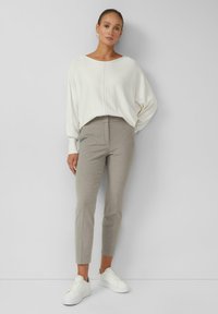 Lekki sweter z kremowym odcieniem o luźnym kroju, zestawiony z dopasowanymi jasnoszarymi spodniami i białymi sneakersami. Prosty design, gładka tekstura.