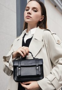 Borsa a mano in pelle nera con manico superiore, chiusura a pattina e hardware argento. Texture liscia e forma rettangolare con logo impresso.