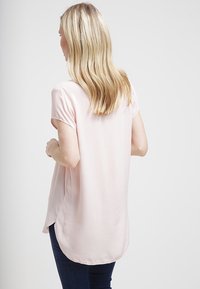 Světle růžová blůza s uvolněným střihem, krátkými rukávy a zakřiveným lemem, vyrobená z hladké, lehké látky.