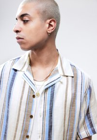 Short-sleeve button-up shirt in textured white fabric with blue, brown, and beige vertical stripes. Features a pointed collar and wooden button.