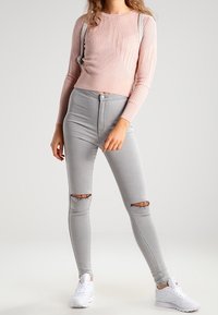 Ljusrosa ribbad tröja med långa ärmar, matchad med grå tajta jeans med knäskärningar och vita sneakers.