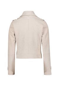 Beskåret beige jakke med en struktureret krave, lange ærmer og knapdetaljer. Har synlige syninger og et minimalistisk design.