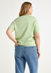 Top a maniche corte di maglia verde chiaro, vestibilità comoda, con texture semplice, abbinato a jeans in denim azzurro chiaro a vita alta con tasche posteriori.