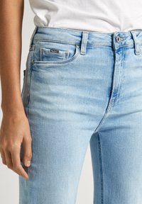 Ljust blå denimjeans i slim fit, med liten framficka, bältesöglor och knäppning med mässingsknapp. Texturerad tyg med blekningar.