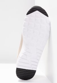 Bílá podrážka tenisky s texturovaným vzorem běhounu. Svršek je béžový s hladkým povrchem. Na podrážce je značka.