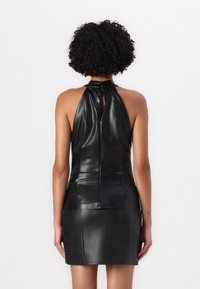 Top halter in pelle nera con un design aderente, texture liscia e dettaglio a occhiello sul retro. Il capo si estende in una mini gonna elegante.