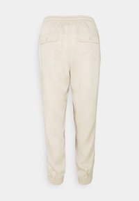 Beige elastische Hosen mit Knopfverschluss an den hinteren Klappentaschen und elastischen Bündchen, von hinten vor einem weißen Hintergrund präsentiert.