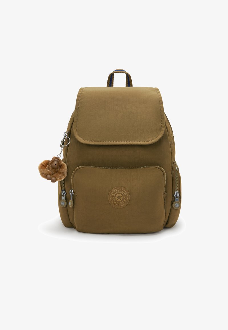 Mochila de tela marrón con cierre de solapa, bolsillos con cremallera y un llavero con un charm de mono. Presenta un logo en la parte frontal y una superficie texturizada.