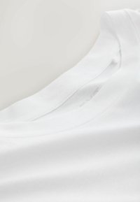 Bílé bavlněné tričko s kulatým výstřihem, má hladkou strukturu a čisté švy podél límce a ramenních švů.