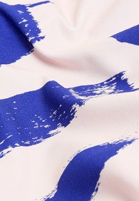 Pohjana oleva puuvillakangas, jossa on leveitä, rohkeita sinisiä siveltimen jälkiä vaaleanpunaisella taustalla, esittelee sileän pinnan ja eloisat värit.