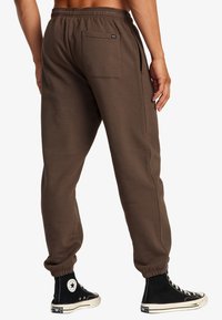Braune Sweatpants mit elastischem Bund, Seitentaschen und einer Gesäßtasche. Gefäßte Bündchen und eine weiche Textur sind sichtbar.