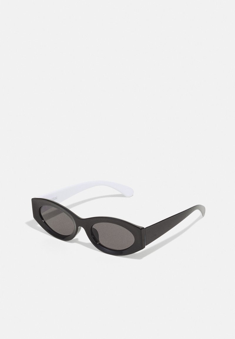 Juodos ovalo formos saulės akinių su blizgiu paviršiumi ir storiu rėmu; balti ratlankiai palaipsniui siaurėja, turi tamsius lęšius.