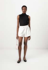 Black sleeveless top, white drawstring shorts, black flats, and a small pink handbag. Smooth texture, fitted design, and casual style.
