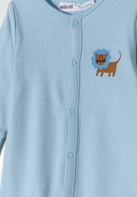 Un mameluco azul claro hecho de suave algodón, con un aplique de león en marrón y azul claro. Tiene un cierre de botones y un cuello redondo.