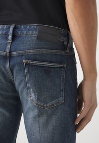 Mörkblå denimjeans med en slät textur, med orangea sömmar, en svart präglad logopatch på midjebandet och en design för bakfickan.