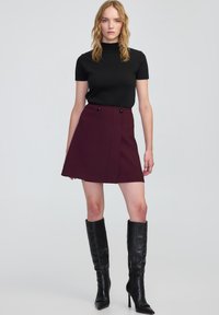 Zwarte korte mouwen top met een ribbelstructuur, gecombineerd met een bordeauxrode A-lijn rok met twee knopen bij de taille en kniehoge zwarte laarzen.
