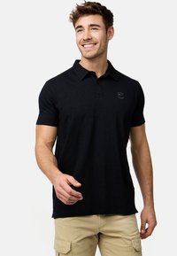 Sort polo skjorte med krave, korte ærmer og et lille logo på brystet. Lavet af blødt stof, med en afslappet pasform og sideslidser.