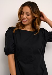 Robe noire avec de courtes manches bouffantes, décolleté carré et détails froncés aux manches, fabriquée en tissu léger et lisse.