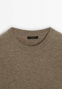 Pull en maille marron avec un col rond. Dispose d'une texture douce et de bords côtelés. Comprend une étiquette noire à l'intérieur du col.