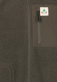 Gilet en polaire vert olive foncé, doté d'une poche poitrine zippée et d'accents cousus. Texture côtelée et logo sur la poitrine.