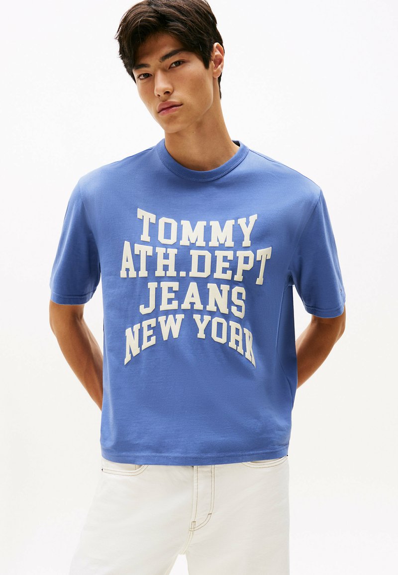 Niebieska bawełniana koszulka z krótkim rękawem i okrągłym dekoltem, z dużym białym nadrukiem "TOMMY ATH. DEPT JEANS NEW YORK." Miękka w dotyku.