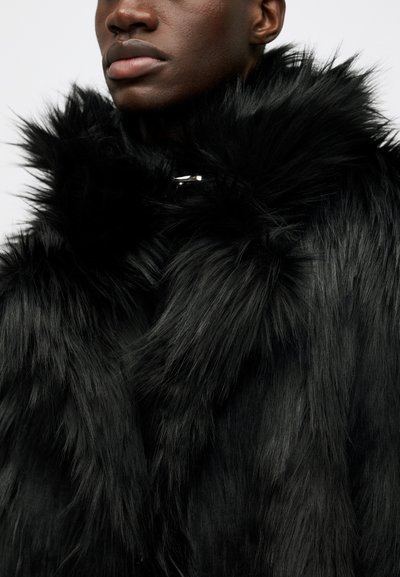 Černý kabát z umělé kožešiny s vysokým límcem, vrstvenou strukturou a charakteristickým stříbrným kováním pro zapínání.
