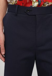 Pantalones azul marino fabricados con tejido texturizado, que cuentan con un cierre de un solo botón y un frente plano con bolsillos laterales.