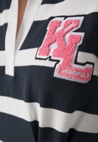 Svartvitt randig polo med en rosa frotté "KL" logotypapplikation, som har en klassisk krage och en texturerad tyg.