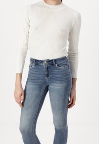 Top blanco de manga larga con textura acanalada y un patrón geométrico, combinado con jeans ajustados azul claro que presentan un diseño clásico de cinco bolsillos.