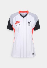 Biała koszulka piłkarska z czarnymi i szarymi akcentami, w paski, z pomarańczowym kołnierzem i detalami po bokach, z logo Nike i herbem Liverpoolu.