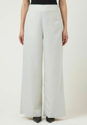 Kvinde iført lysegrå bukser med høj talje og vide ben, kombineret med sorte spidse hæle og en sort top, der er stukket ned.