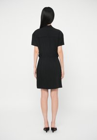 Μαύρο φόρεμα με ρίγες και κοντό μανίκι, με ζώνη στη μέση και ίσιο στρίφωμα. Λείο ύφασμα με δομημένο γιακά και ελάχιστες λεπτομέρειες.