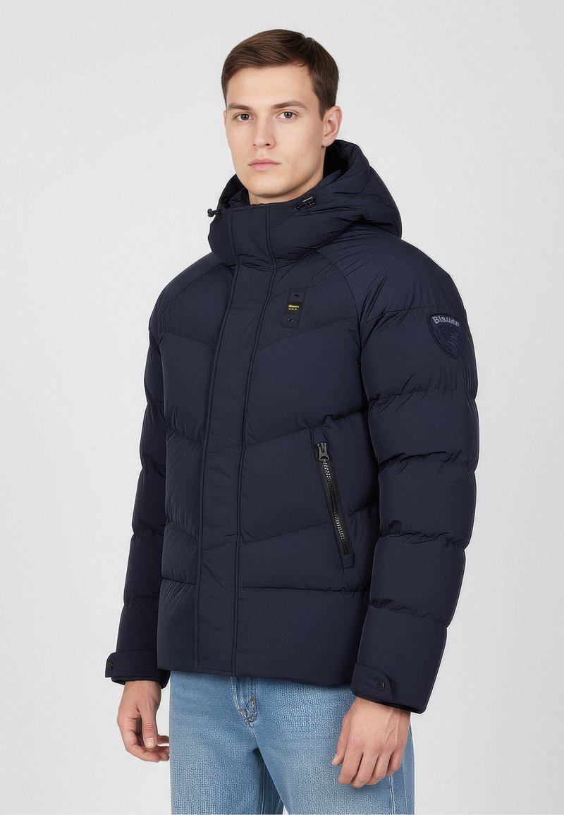 Granatowa kurtka puchowa z wysokim kołnierzem i kapturem. Posiada zapinane na zamek boczne kieszenie, pikowaną teksturę oraz naszywkę z logo na lewym ramieniu.