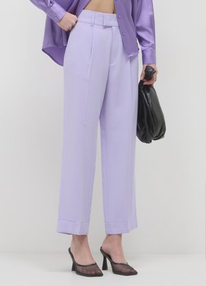 Pantaloni a vita alta color lavanda chiaro realizzati in tessuto liscio, con pieghe frontali, gambe larghe e orlo risvoltato. Indossati con accessori neri.