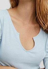 Světle modrý žebrovaný top s širokým, kulatým výstřihem a detaily ve tvaru klíčové dírky, s krátkými rukávy a mírně fitted střihem.