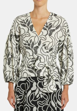 Donna che indossa una blusa avvolgente con motivo astratto bianco e nero e maniche a sbuffo, annodata in vita, abbinata a una gonna con motivo coordinato.
