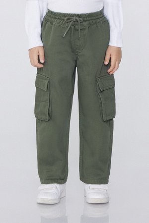 Enfant portant un pantalon cargo vert avec des poches latérales et des baskets blanches, debout les mains détendues le long du corps.