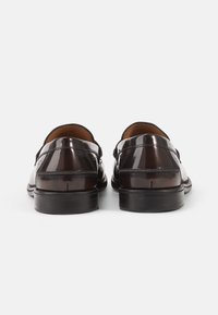 Mocasines de cuero charol marrón oscuro con forma redondeada, textura suave, forro de cuero y suelas de goma negra, exhibiendo un hardware mínimo.
