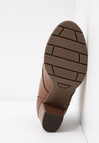 Brązowa skórzana podeszwa buta z teksturowanym gumowym gripem. Posiada segmentowy wzór bieżnika oraz oznaczoną wielkość 37. Lekko wygięty design obcasa.