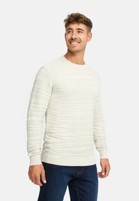 Maglione beige chiaro con texture e righe orizzontali, scollatura rotonda e maniche lunghe, abbinato a jeans blu scuro.