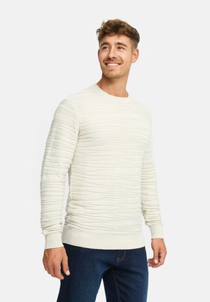 Lys beige struktureret sweater med horisontale ribber, rund halsudskæring og lange ærmer, parret med mørkeblå jeans.