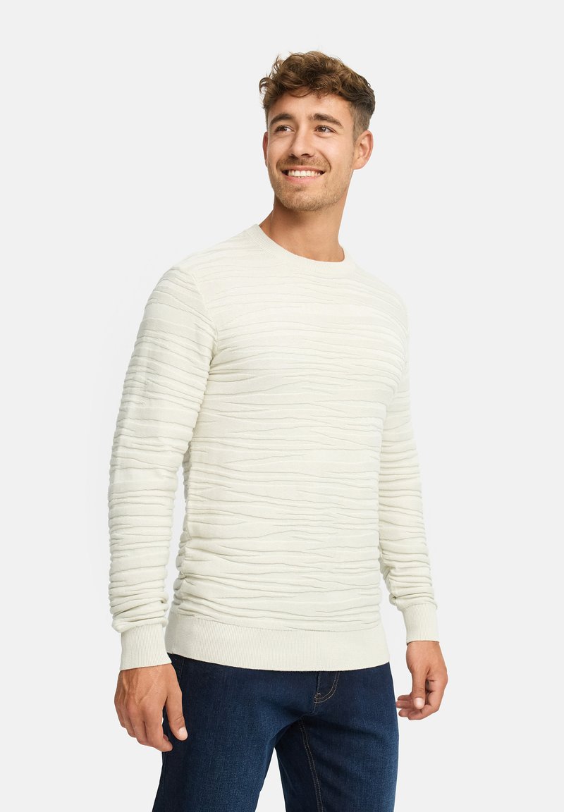 Maglione beige chiaro con texture e righe orizzontali, scollatura rotonda e maniche lunghe, abbinato a jeans blu scuro.