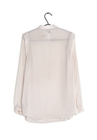 Camicia bianca a maniche lunghe in tessuto satinato semi-trasparente, con polsini a bottone, orlo arrotondato e colletto classico, appesa a un gancio nero.