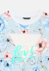 Short-sleeve, light blue floral t-shirt with pink and blue flowers, green "Love" graphic, and triangle logo. Cotton material, ribbed collar.