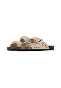 Sandales en suède beige avec perforations, deux sangles réglables avec boucles en or, et une semelle texturée marron foncé.