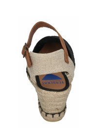 Sandal de espradrille con parte superior de tela trenzada beige, correa de cuero marrón, acentos negros y un tacón de yute trenzado con suela de goma.