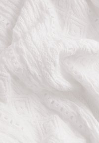 Tissu blanc texturé avec un motif géométrique comprenant des losanges et des nervures verticales. Aspect doux, léger et légèrement transparent.