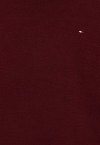 Maglione in borgogna a maglia con superficie testurizzata; presenta un piccolo emblema con marchio in rosso, bianco e blu sulla parte superiore sinistra.