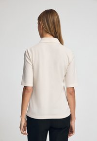 Cr�ème-kleurige polo met korte mouwen, gemaakt van een gladde stof. Voorzien van een klassieke kraag en een rechte zoom.